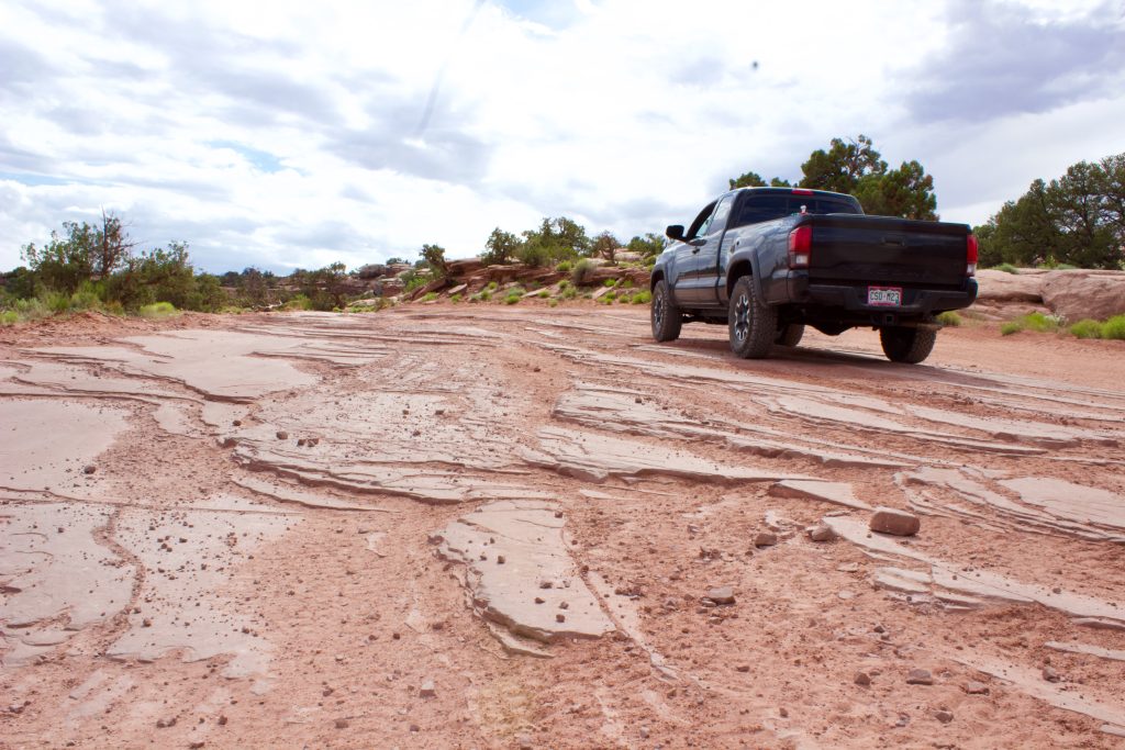 Stock black Toyota Tacoma TRD Off-Road wheeling over slick rock on Moab's Gemini Bridges 4x4 trail.