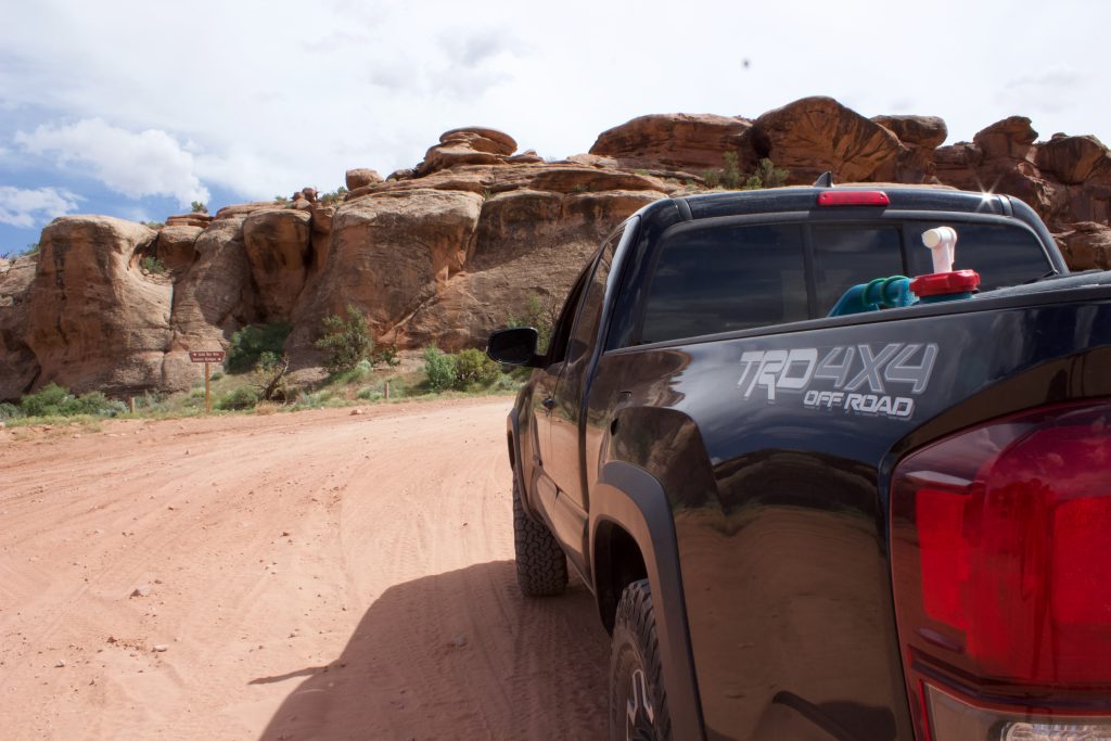 Black Toyota Tacoma facing canyon wall on Gemini Bridges Moab off-roading trail packed with a water jug in the truck bed.