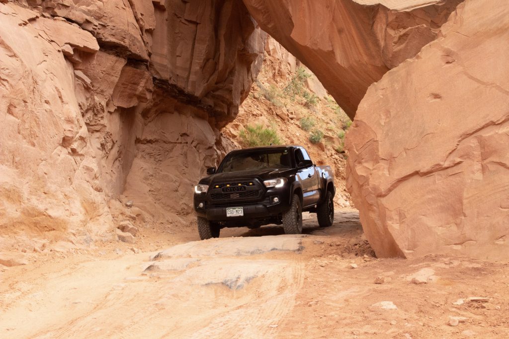 Black Toyota Tacoma underneath fallen boulders balanced by the walls of Long Canyon off-roading trail.