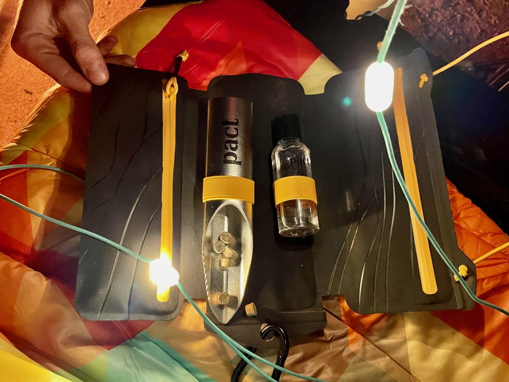 Colorful background and lit-up string lights strung across a PACT Outdoors Bathroom Kit aluminum shovel with mycelium tablets displayed on the tailgate of a Toyota Tacoma.