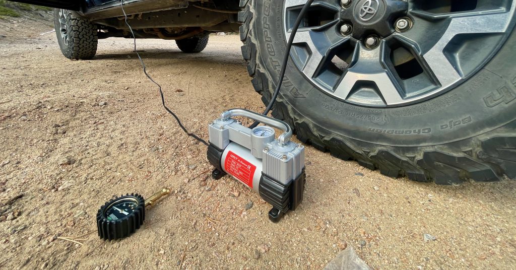 Wheel of a Toyota Tacoma inflating on a dirt road next to a Rhino USA deflator gauge which makes a great affordable overland accessory or gift.