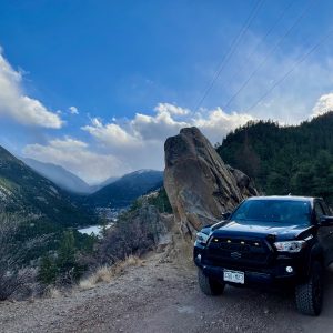 Magnetic black Toyota Tacoma TRD Off Road viewed from the front on a 4x4 trail on the side of a mountain overlooking mountains and a lake in Colorado.
