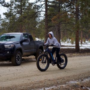 Woman riding on a blue Rattan Sequoia ebike on a trail by a Toyota Tacoma.